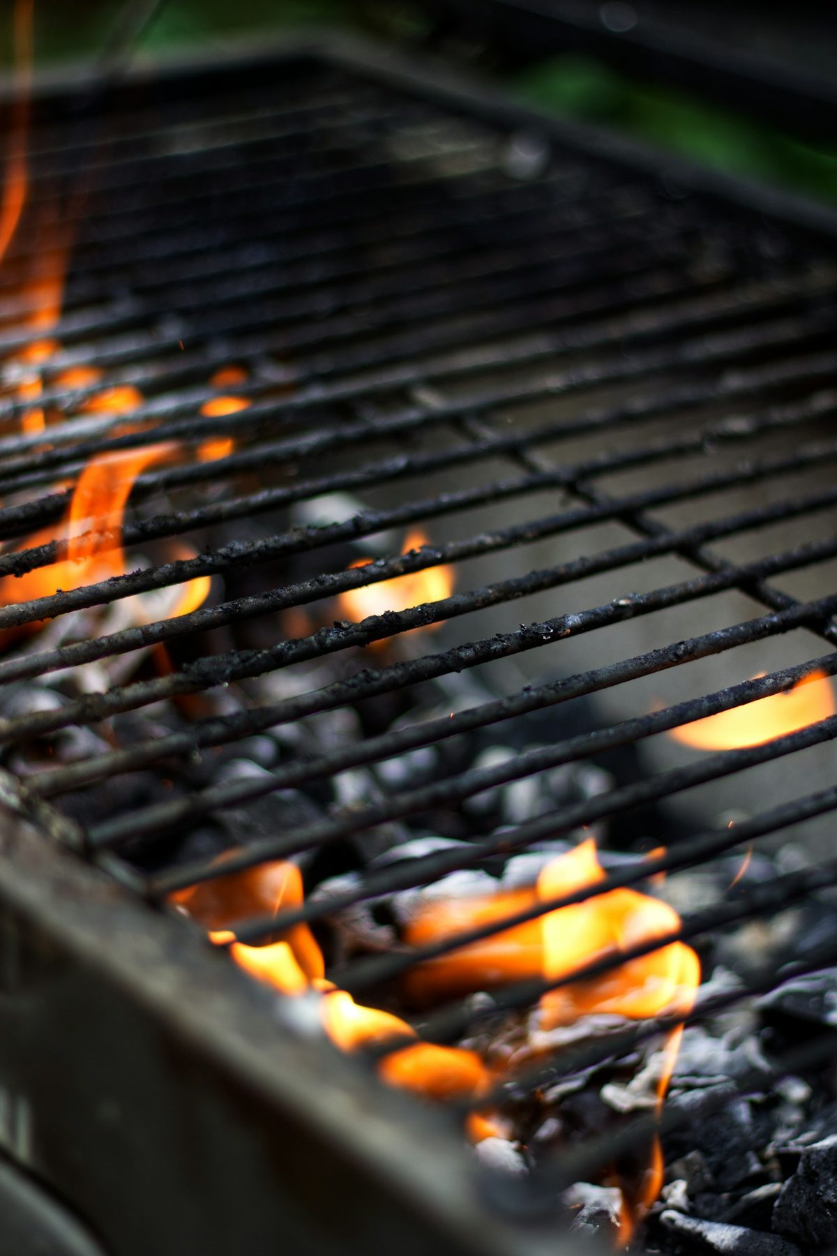 Glowing coals and flame under a steel grill grate