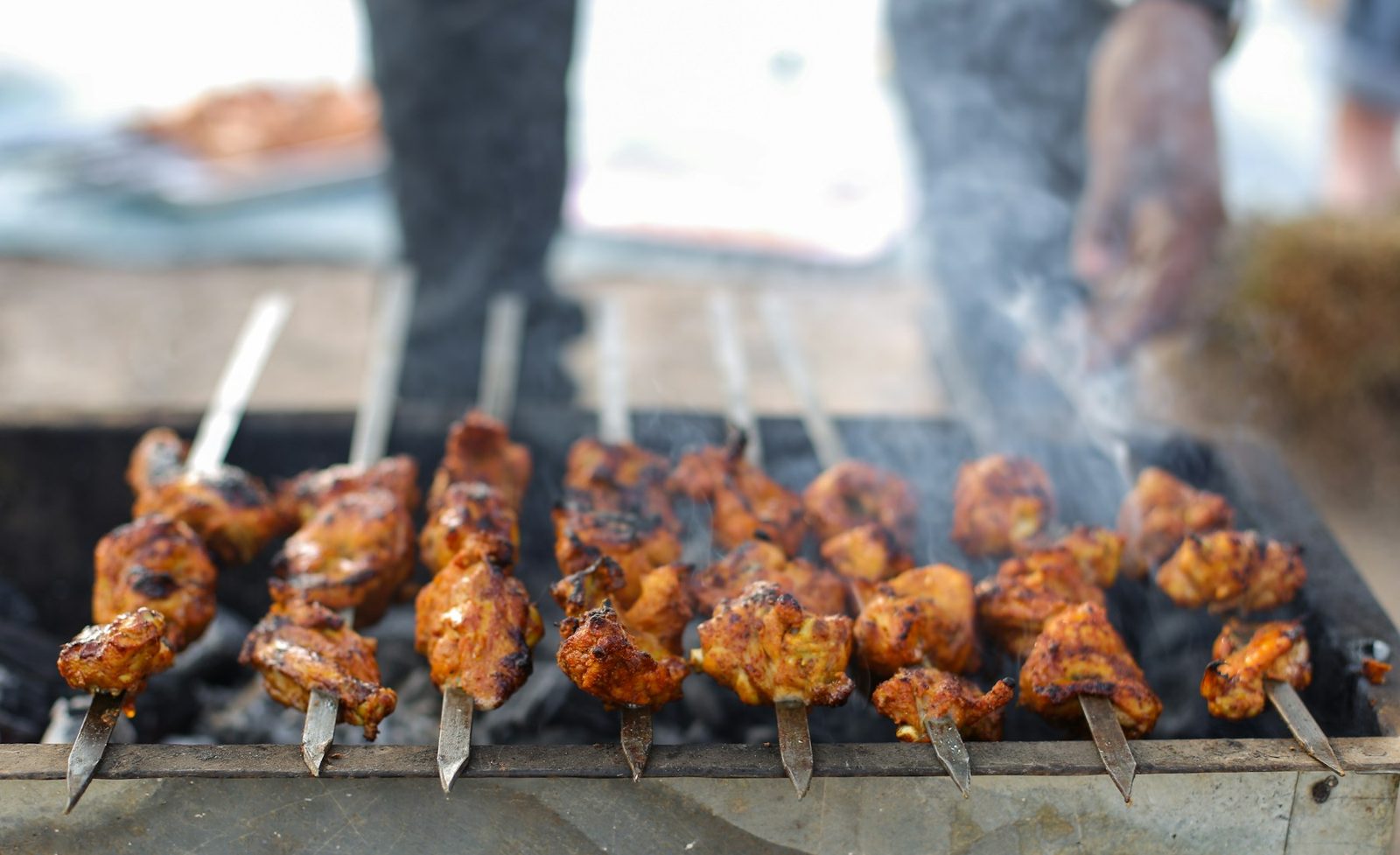 Skewers of red-glazed meat over a smoking charcoal grill