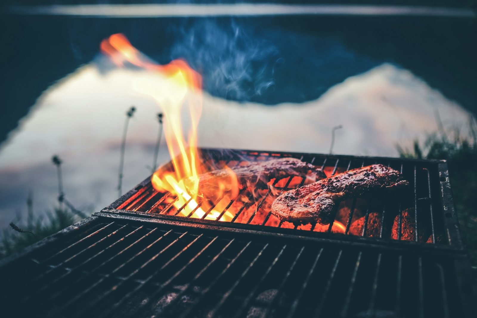 A steak on a grill grate with flames rising around it