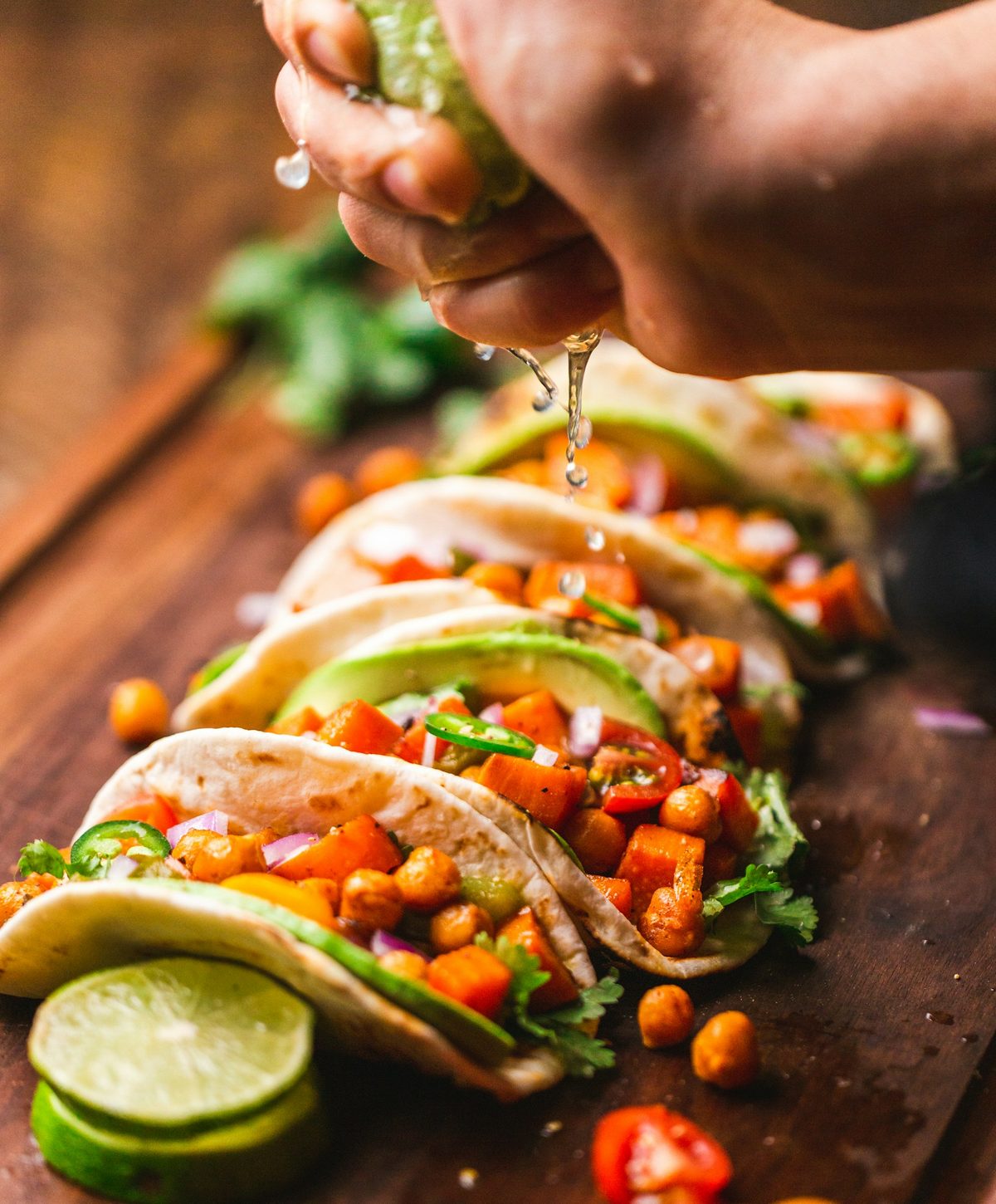 Three soft tacos piled with grilled filling, a hand squeezing lime over them