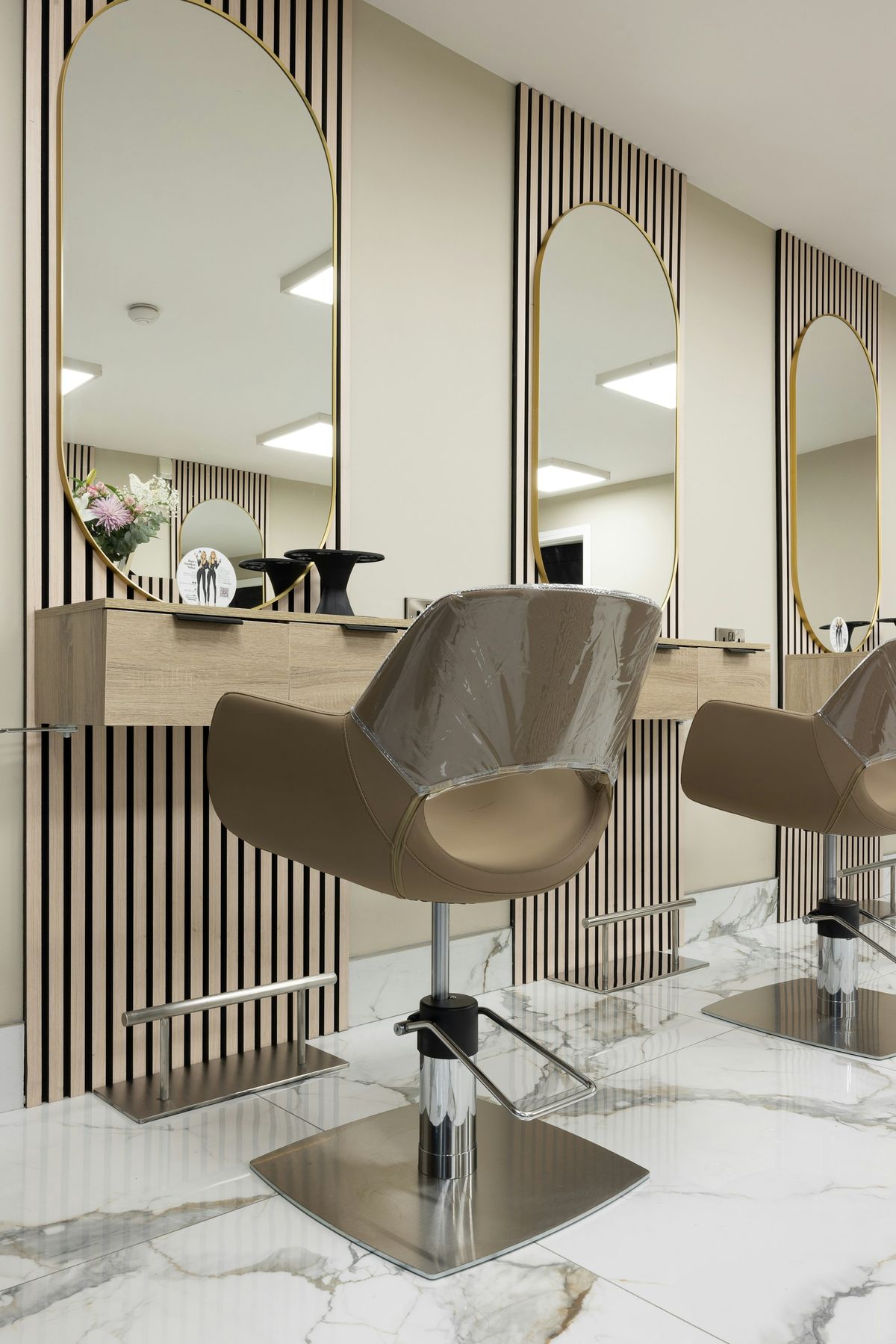 A row of tall arched mirrors with brass frames above pale oak counters and styling chairs.