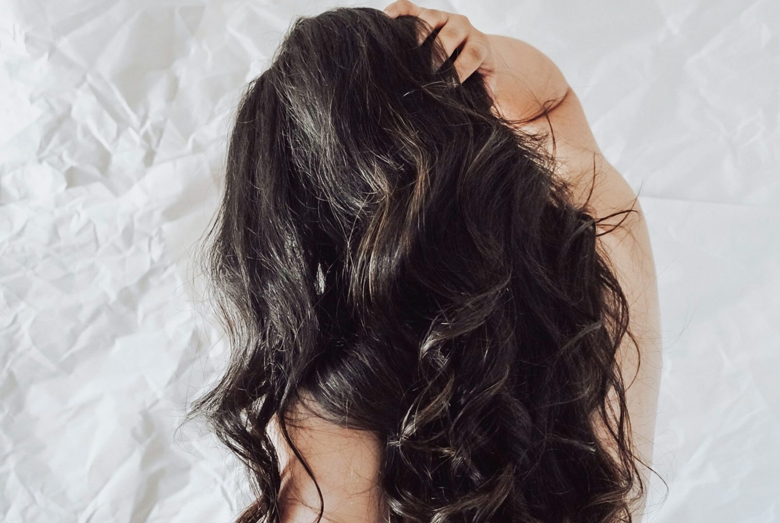 Long dark curls seen from behind against pale crumpled linen.