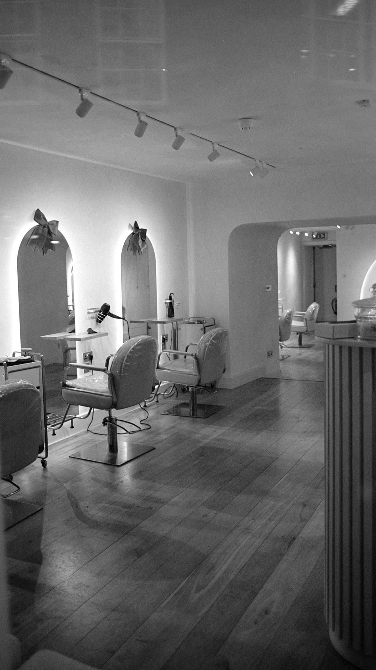 A quiet salon floor in black and white: arched mirrors, styling chairs and a long pale floor.