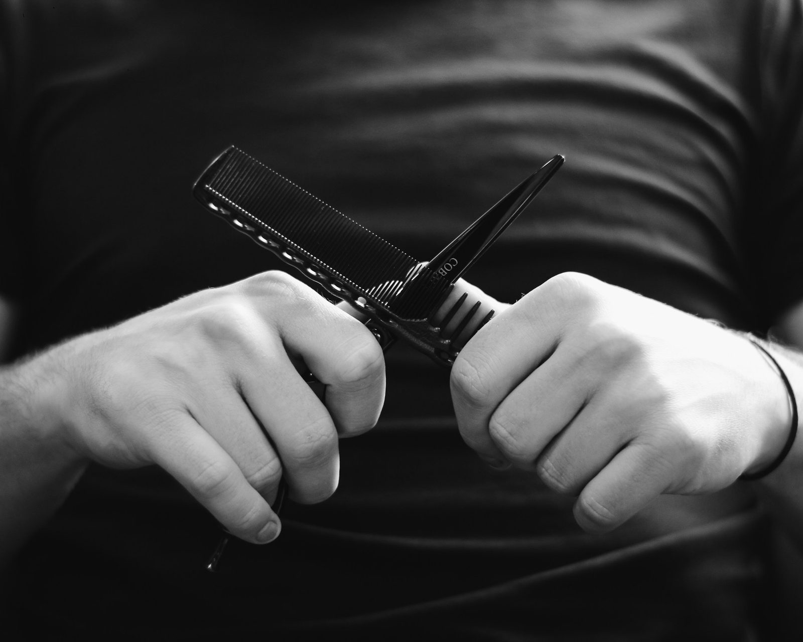 Two hands crossing a pair of scissors and a cutting comb, in black and white.