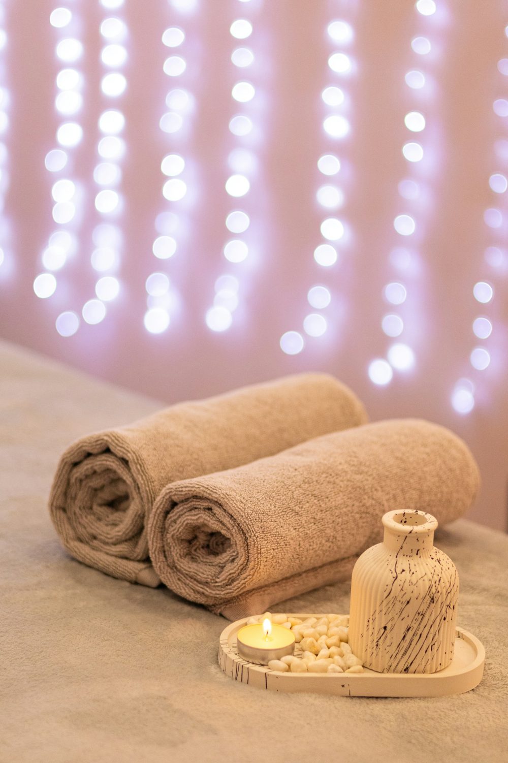 Rolled towels, a small vase and a candle on a treatment table