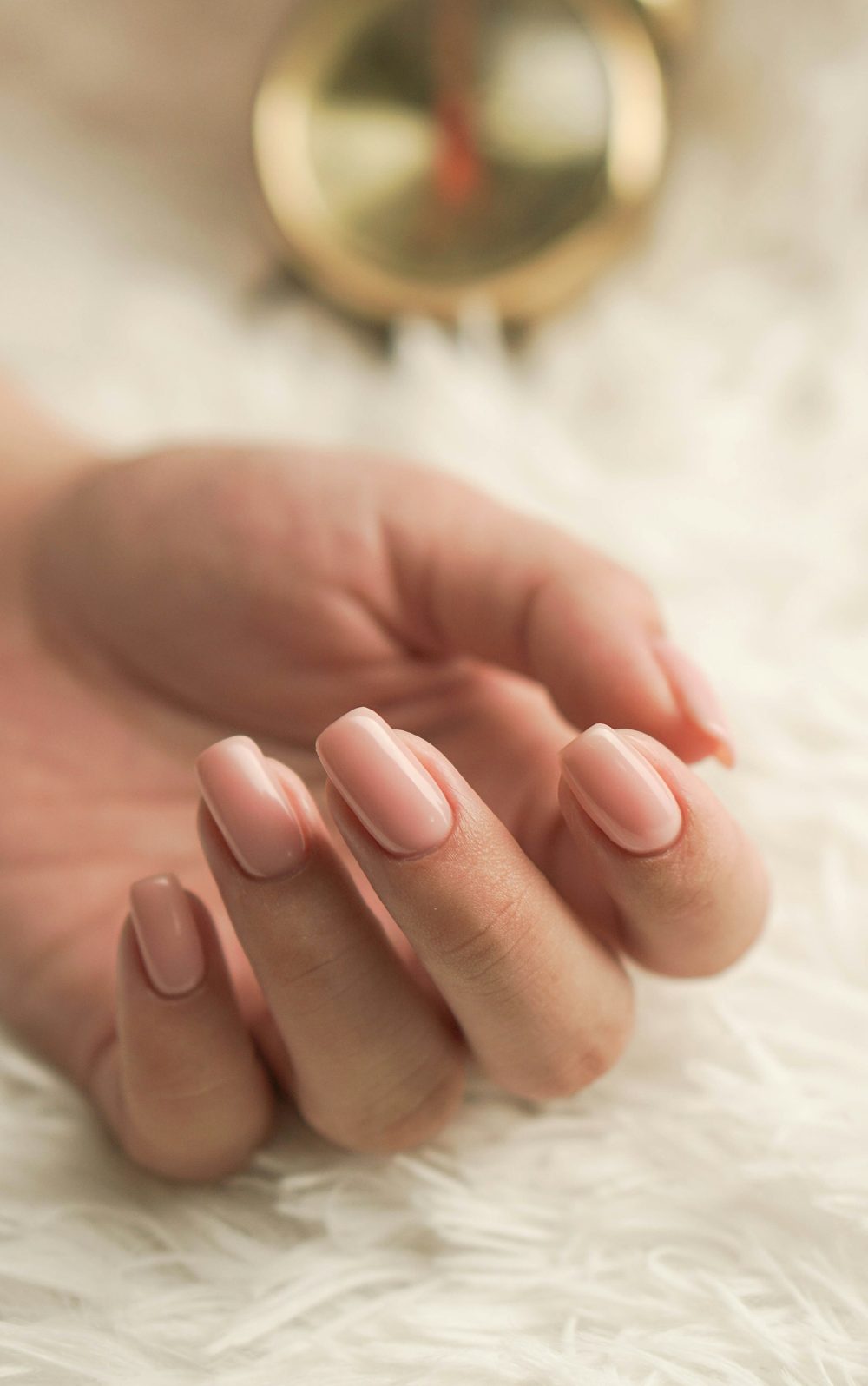 A hand with light pink manicured nails resting on a soft white throw