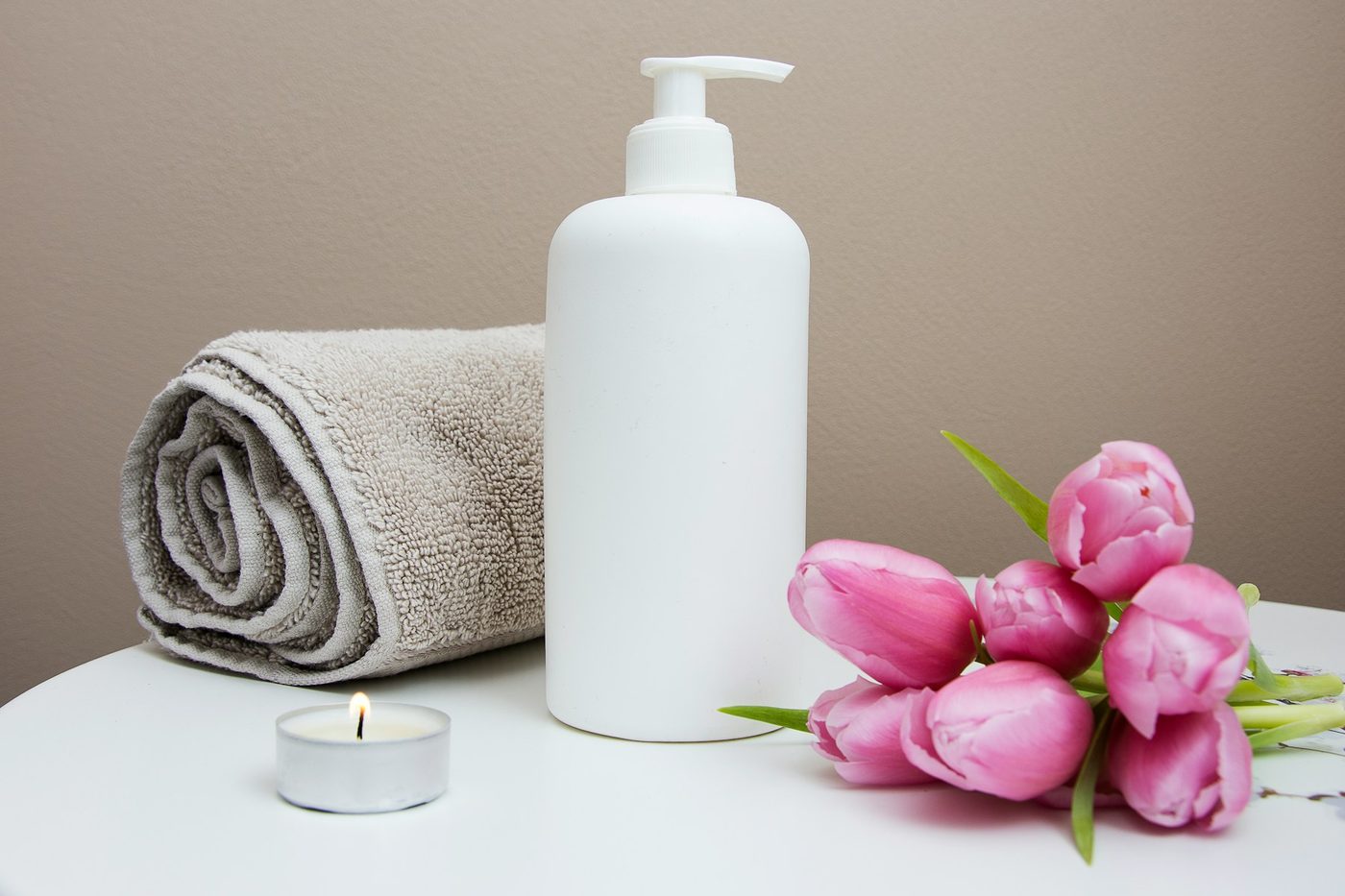 A plain pump bottle beside pink tulips and a folded grey towel