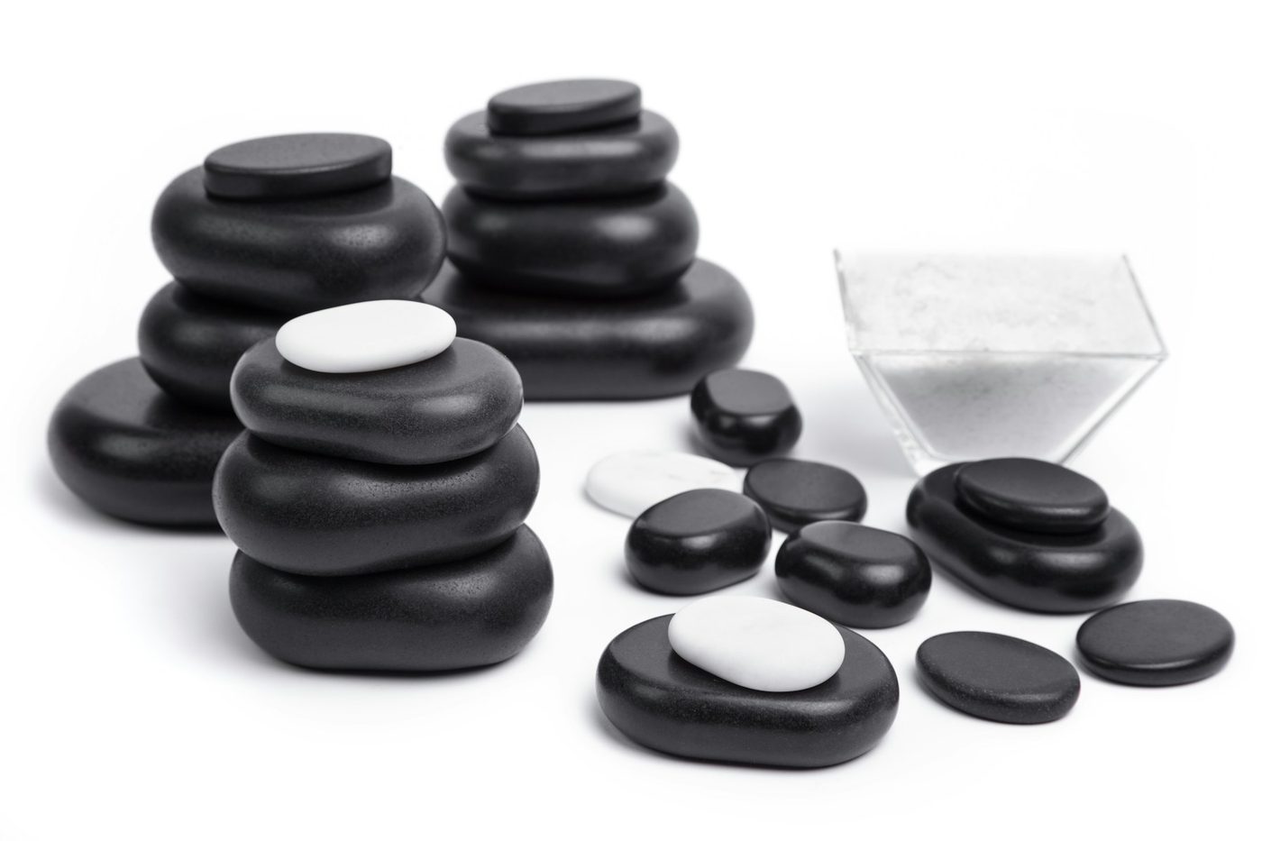 Smooth black massage stones stacked on a white surface