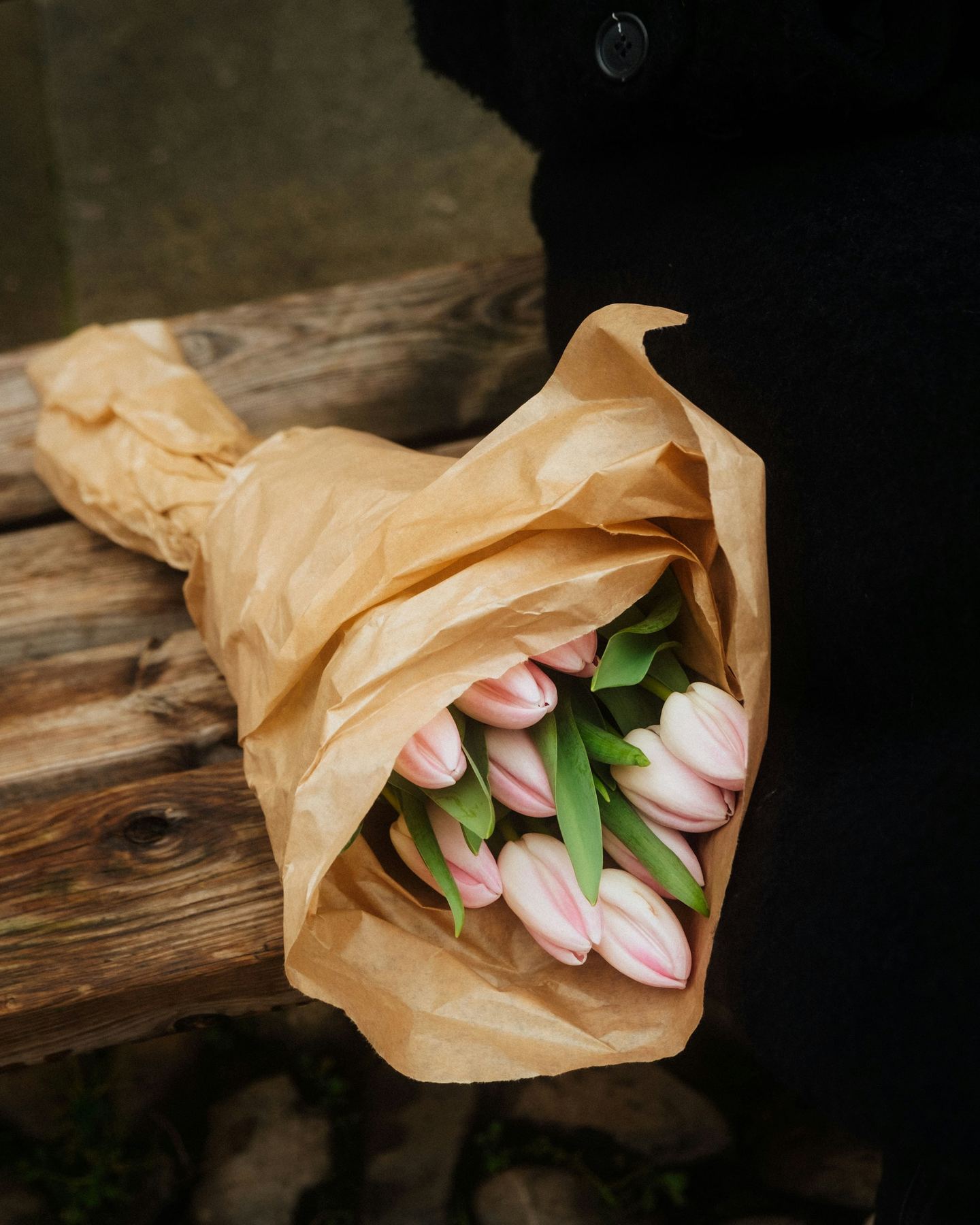 Pale pink tulips wrapped in brown paper, lying on dark wood