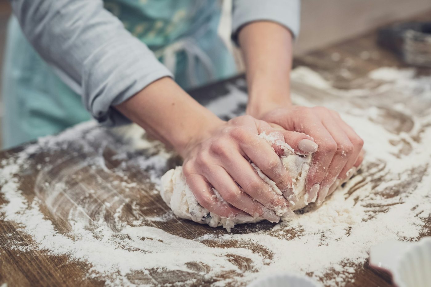 Hands kneading dough on a floury wooden bench