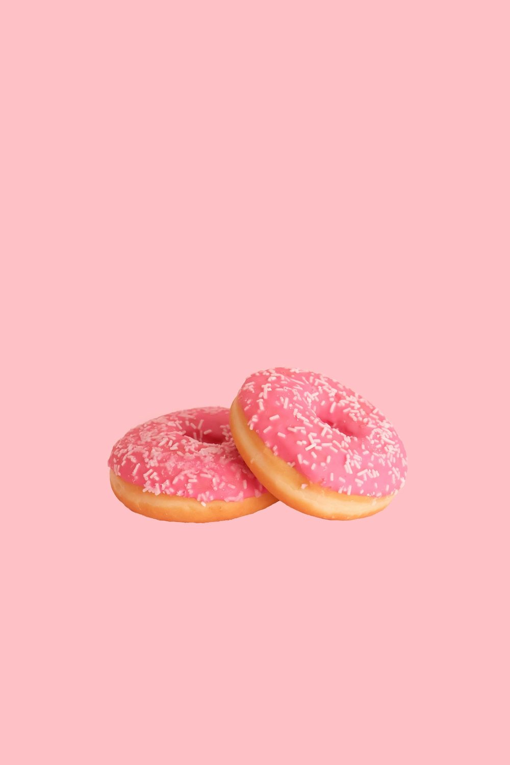 Two pink sprinkle doughnuts on a pink background